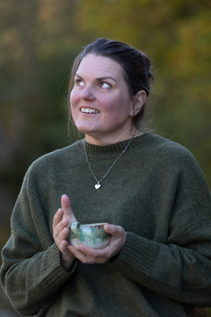 Louise Svendsen står udendørs med en kop i hænderne og ser opad i naturen Det er den teknisk korrekte version.